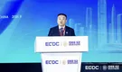 Man speaking at an ECDC and IDEE·SZ branded podium before a blue city skyline backdrop.