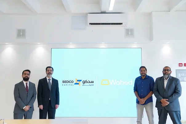 Four men stand before a screen displaying SEDCO Capital and Wahed logos.